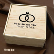 A wooden box with a lid, featuring a graphic of two rings and the text "The Day We Said 'I Do'" printed on it.