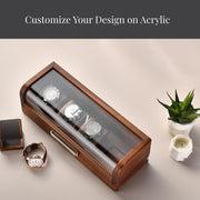 a wooden watch case with four watches inside, placed on a wooden surface alongside a small potted plant and a candle.