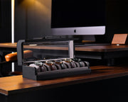 a desk with a computer monitor and a watch in a case
