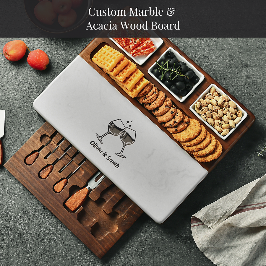 A wooden serving board with a marble top, displaying an assortment of snacks and crackers, as well as a knife set.