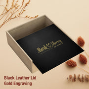 a black leather lid with gold engraving, placed on a wooden surface with dried flowers and pine cones.