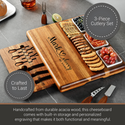 A wooden cheeseboard with a 3-piece cutlery set, featuring a personalized engraving, is displayed on a gray countertop.