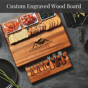 A wooden cutting board with various food items, including grapes, cookies, crackers, and cheese, as well as a set of wooden utensils.