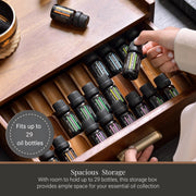 A wooden drawer with multiple compartments, containing various essential oil bottles. A person is reaching into the drawer to select an oil bottle.