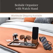 a bedroom with a bedside organizer that includes a watch stand, a pair of sunglasses, a phone, and a tie, all neatly arranged on a tray.