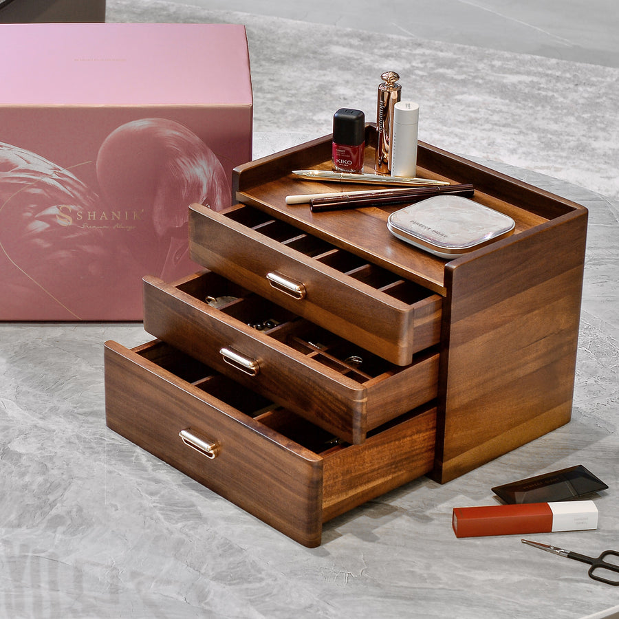 A wooden makeup organizer with three drawers, displaying various makeup items such as a lipstick, eyeshadow palette, and a compact.