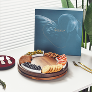 a wooden platter with various snacks and appetizers, accompanied by a blue box with a bird design and the text "Shanik" on it, placed on a white table.