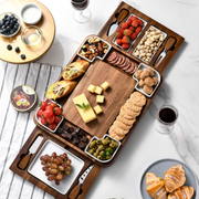 a wooden serving platter filled with various snacks and appetizers, accompanied by wine glasses and other tableware, suggesting a social gathering or a celebration.
