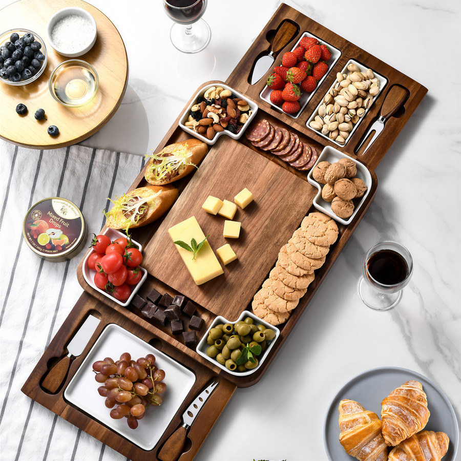 a wooden serving platter filled with various snacks and appetizers, accompanied by wine glasses and other tableware, suggesting a social gathering or a celebration.
