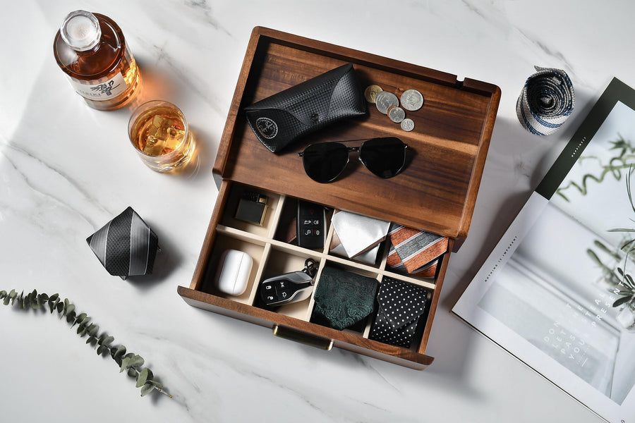 a wooden drawer with various accessories, including sunglasses, a tie, a book, and a bottle of alcohol.