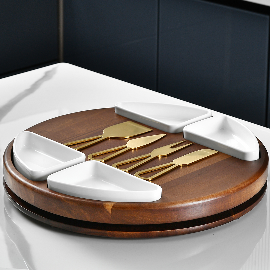 A wooden serving tray with four white ceramic serving dishes arranged on it, along with a pair of gold-colored serving utensils.