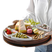 A person is holding a wooden tray filled with various food items, including cheese, grapes, cookies, and olives.