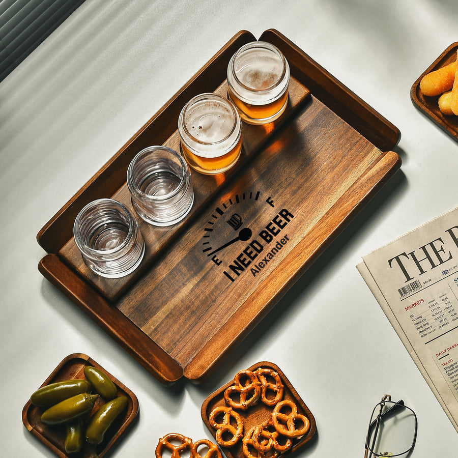 A wooden tray with three glasses of beer, a plate of pickles, and a newspaper on a table.