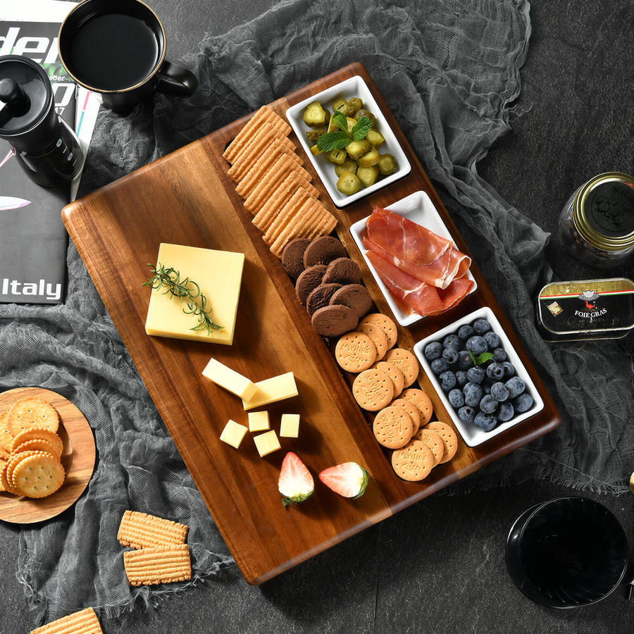 A wooden serving board filled with an assortment of snacks and finger foods, including cheese, crackers, cookies, and fruit, is placed on a gray surface.