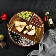 A wooden platter with various cheese slices, grapes, olives, and other snacks arranged on a dark surface.