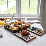 A wooden tray filled with various fruits, breads, and other snacks is placed on a table near a window.