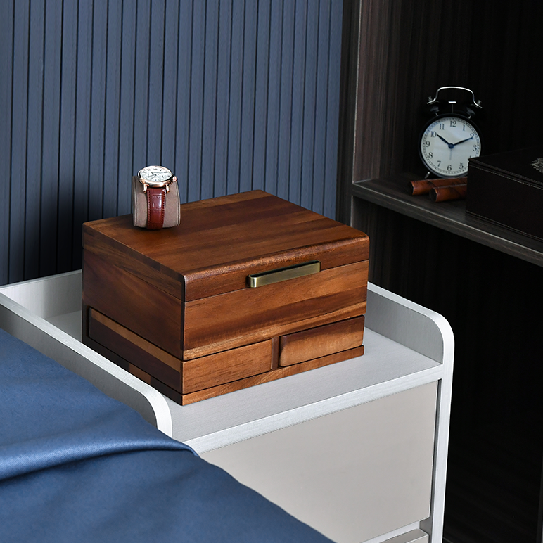 A wooden nightstand with a drawer and a wooden box on top, along with a clock and a watch, is situated in a bedroom setting.