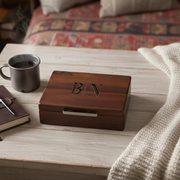 A wooden box with the initials "BN" engraved on it, accompanied by a mug of coffee and a notebook on a wooden surface.
