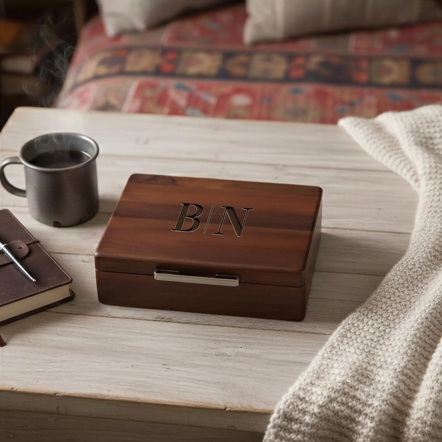 A wooden box with the initials "BN" engraved on it, accompanied by a mug of coffee and a notebook on a wooden surface.