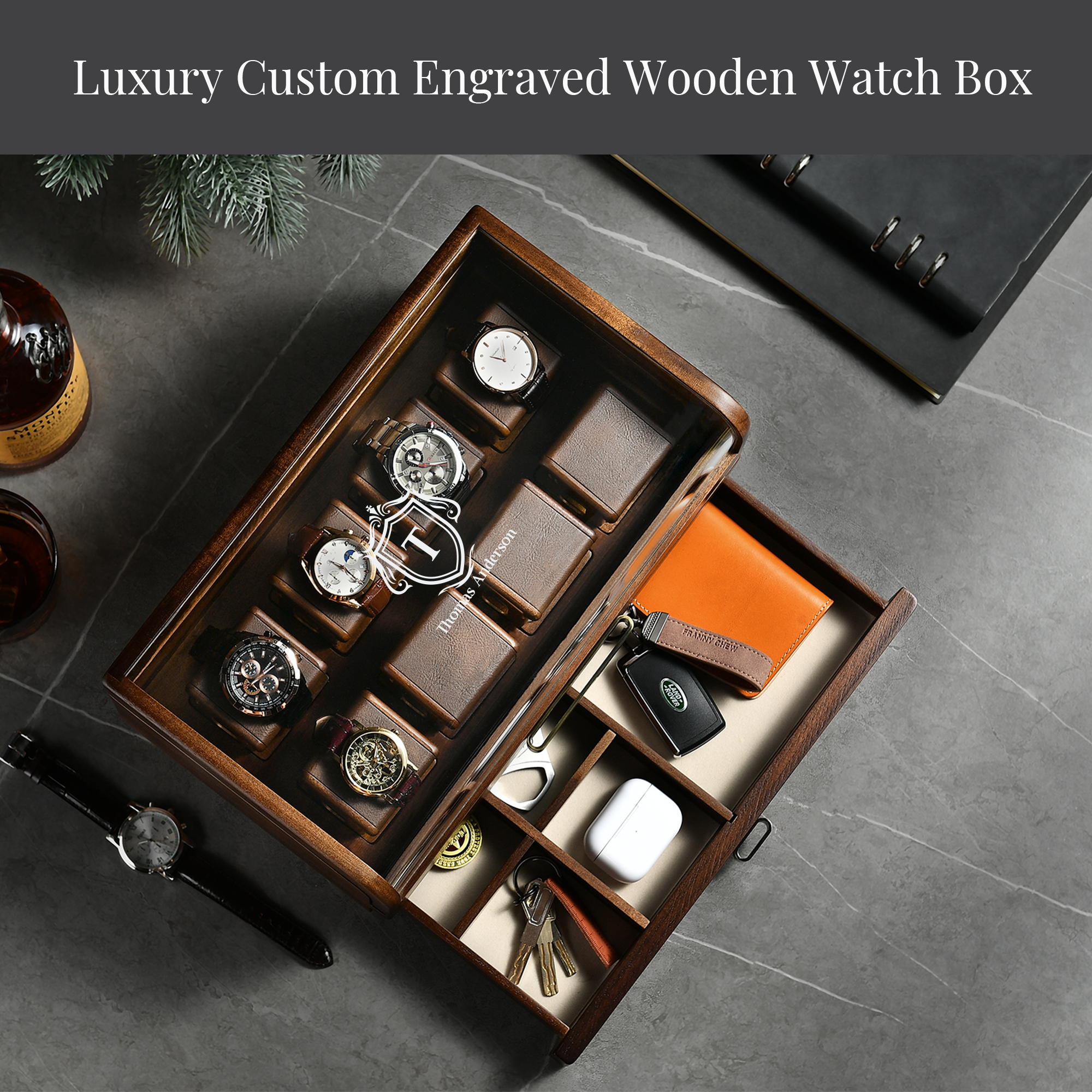 A luxury custom engraved wooden watch box containing various watch-related items, such as a watch, keys, and a wallet, placed on a marble surface.