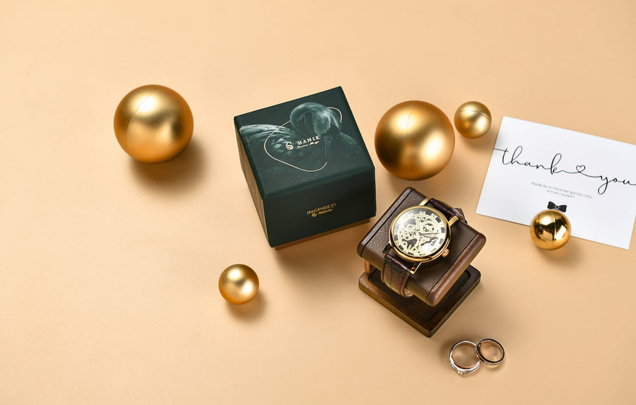 a watch, a box, and some gold balls arranged on a beige background.