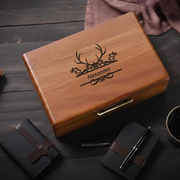 A wooden box with a personalized name engraved on it, accompanied by a pen, a notebook, and a mug on a wooden surface.