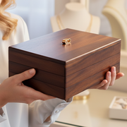 A person is holding a wooden box with a gold ring on top, possibly in a jewelry store or similar setting.