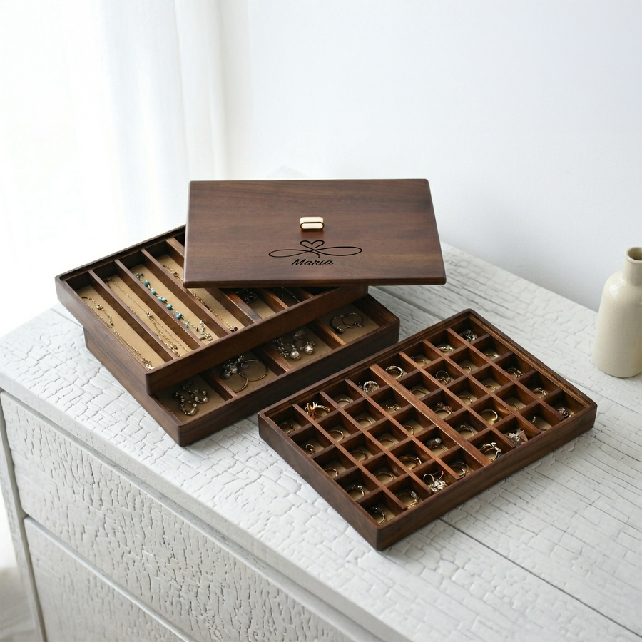 A wooden jewelry box with multiple compartments, displaying various pieces of jewelry, sits on a white surface.