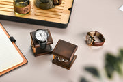 a collection of luxury items, including a wooden box with a watch inside, a brown leather watch, and a glass of tea on a wooden tray.