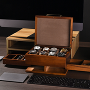 A wooden watch box containing multiple watches is placed on a desk, with a computer keyboard and other office supplies visible in the background.