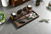 A wooden tray with various accessories, including a pair of sunglasses, a wallet, a keychain, and a car key, arranged on a marble surface.