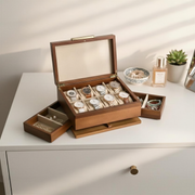 A wooden jewelry box with multiple compartments, displaying various watches and jewelry items, placed on a white dresser.