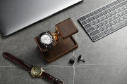 a collection of luxury items, including a wristwatch, a wooden stand, a keyboard, and a pair of cufflinks, all arranged on a gray surface.