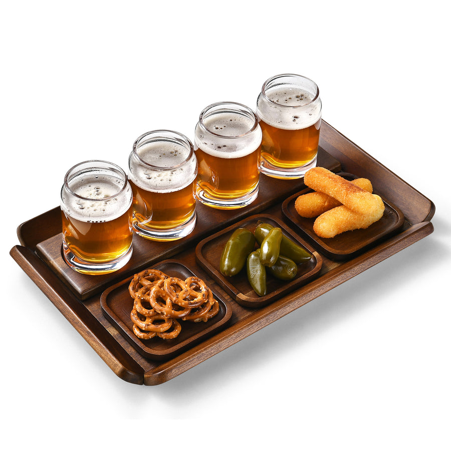A wooden tray with four glasses of beer, two small plates of snacks, and two small plates of pickles.