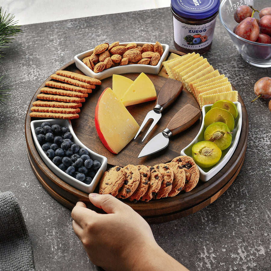 A wooden platter filled with various snacks, including crackers, cheese, blueberries, cookies, and a knife, is displayed on a table.