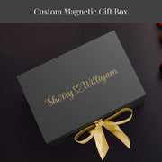 A gray gift box with a gold ribbon tied around it, placed on a dark surface.