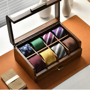 A wooden tie box with nine compartments, each containing a different colored tie, is displayed on a wooden surface.