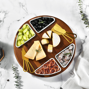 A wooden platter with various cheese slices, grapes, olives, and other appetizers arranged on a marble surface.
