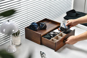 A person is organizing a wooden drawer with multiple compartments, pulling out a tie from one of the compartments.