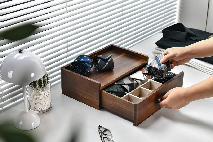 A person is organizing a wooden drawer with multiple compartments, pulling out a tie from one of the compartments.
