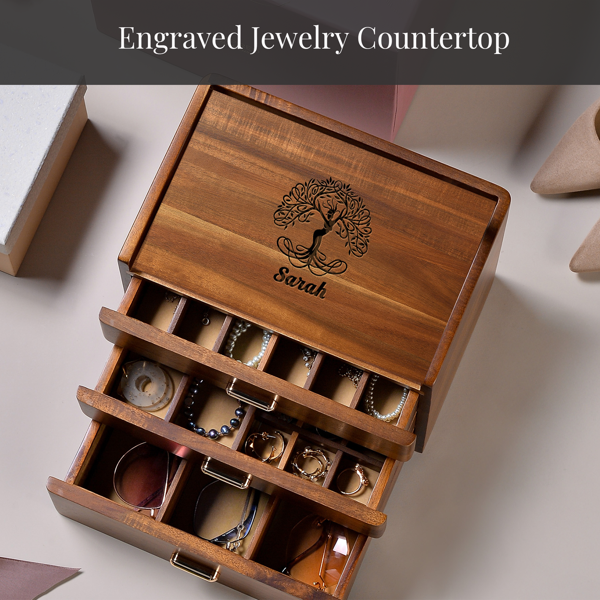 A wooden jewelry box with three compartments, each containing various pieces of jewelry. The box has a tree-like design on the lid and the name "Sarah" engraved on it.