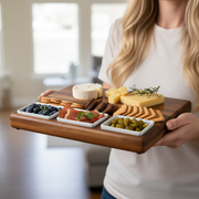 A woman holds a wooden tray filled with an assortment of cheese, crackers, and other appetizers, ready to be enjoyed.