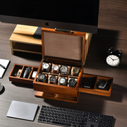 a wooden watch storage box with multiple compartments, containing various watches, placed on a desk alongside a computer keyboard, a clock, and other office supplies.
