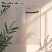 a medication schedule planner hanging on a wall, with a plant in the foreground.