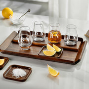 a wooden tray with four glasses, each containing a different colored liquid, arranged on a white surface. There are also lemon slices and a small bowl of salt nearby.