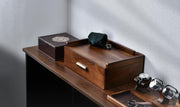a wooden desk with various items on it, including a wooden box, a pair of glasses, and a watch stand.