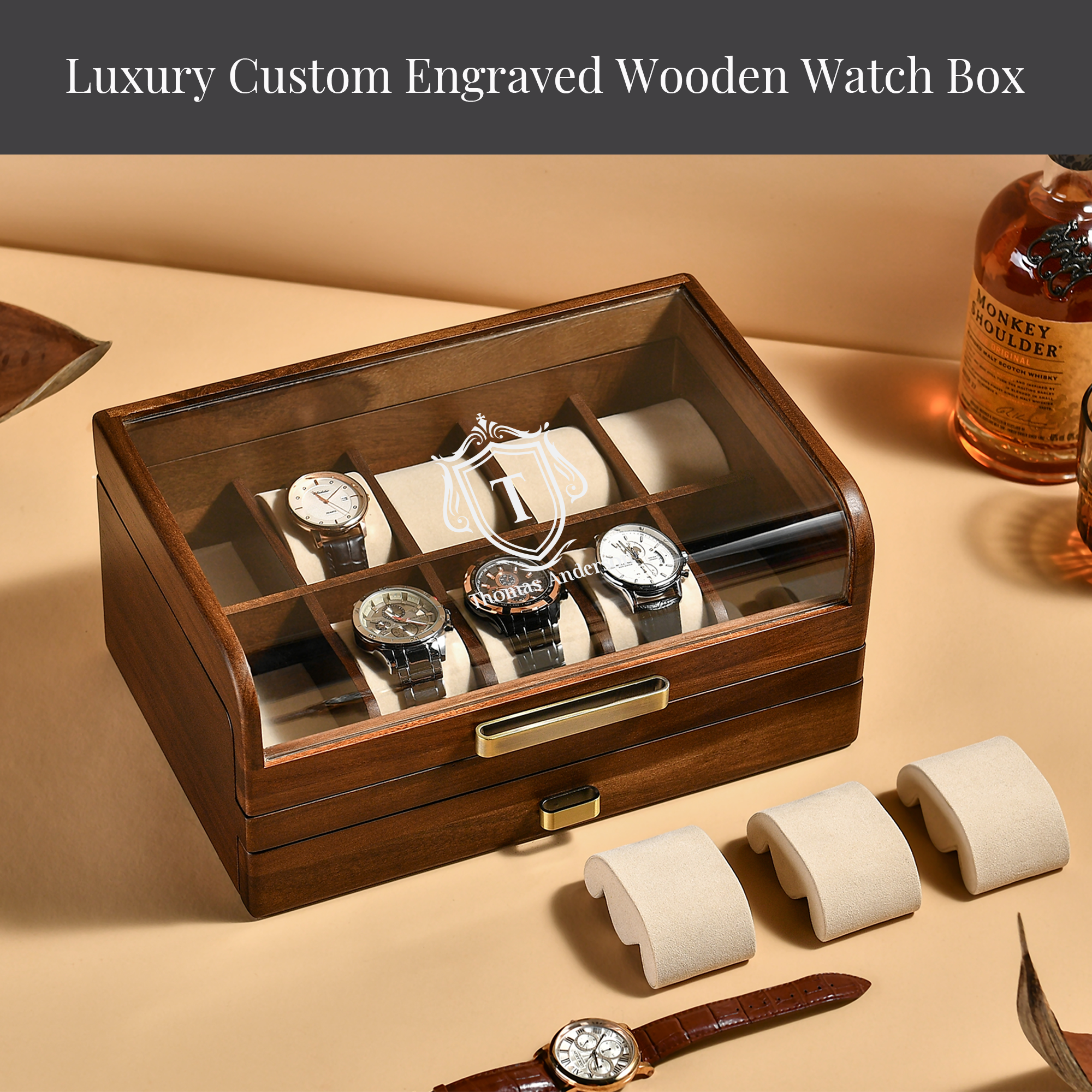 A wooden watch box with multiple compartments, displaying several watches inside. The watch box is placed on a table, with a bottle of whiskey and a leather strap visible in the background.