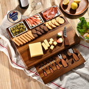 A wooden serving board filled with various snacks and cheese, accompanied by a bottle of wine and a glass of wine on a wooden table.
