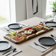 A wooden platter filled with various appetizers, cheeses, crackers, and other finger foods is displayed on a table, accompanied by place settings and utensils.