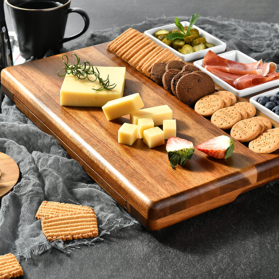 A wooden cutting board displays an assortment of cheese, crackers, and other snacks arranged on a gray cloth.